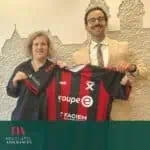 Jolie photo de deux personnes tenant un maillot de football avec l'arrière-plan d'un mur texturé, représentant Neuchâtel Assurances, mettant en avant leur partenariat sportif et leur engagement envers leurs clients.