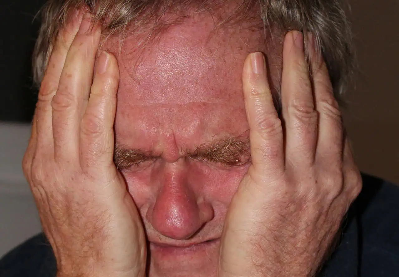 Mains sur visage d'un homme stressé ou anxieux, mettant en évidence le besoin de couverture d'assurance santé ou accompagnement émotionnel.