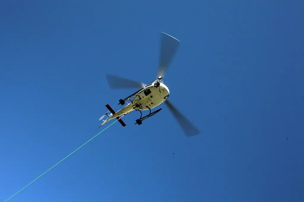 Hélicoptère en vol avec câble de levage contre un ciel bleu clair, symbolisant la sécurité et l'intervention aérienne.