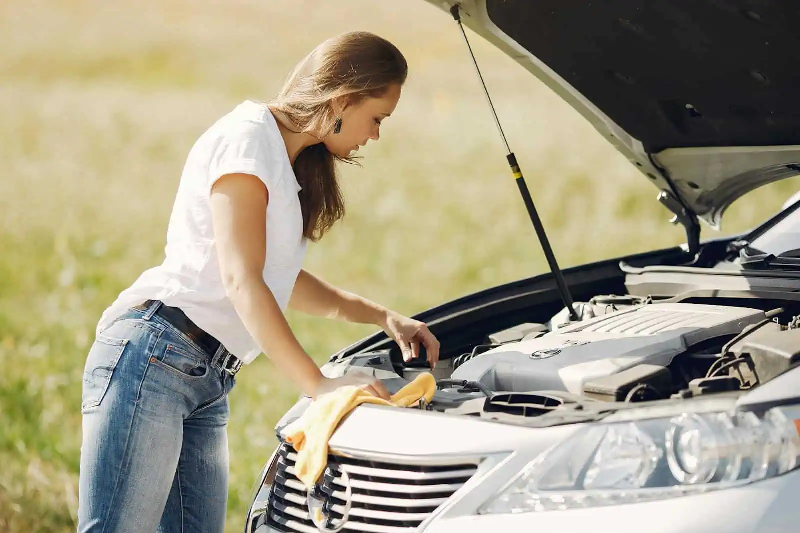 Visage de femmeInspectant le moteur d'une voiture en plein air, lors d'une vérification ou d'une panne, sous un ciel ensoleillé, avec un champ vert en arrière-plan, pour assurer la sécurité et la maintenance de votre véhicule.