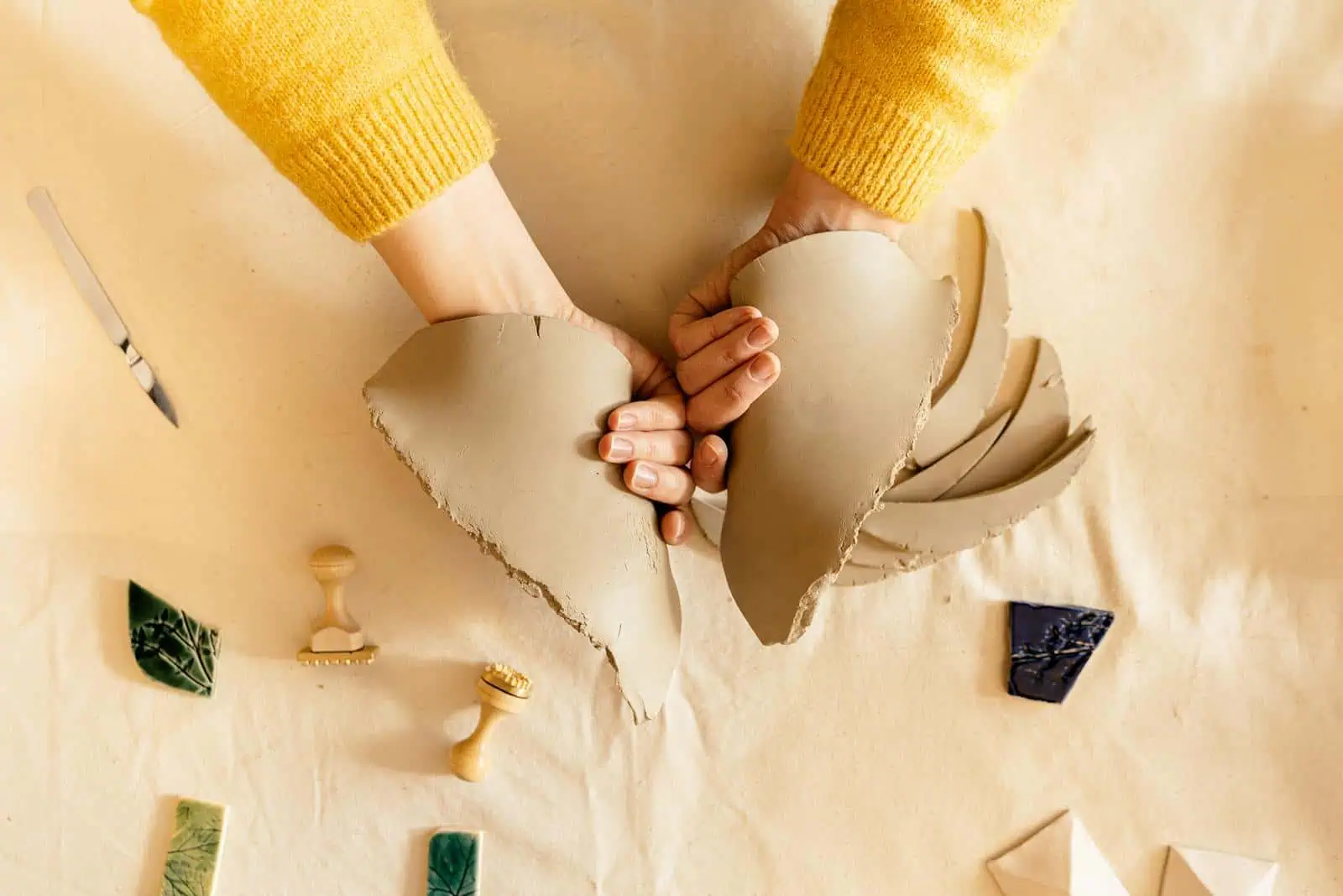 Poinçonnées en céramique craquelée par deux mains, symbolisant la solidité et la fiabilité des assurances Neuchâtel, avec outils et échantillons en arrière-plan, représentant la personnalisation et la qualité du service.