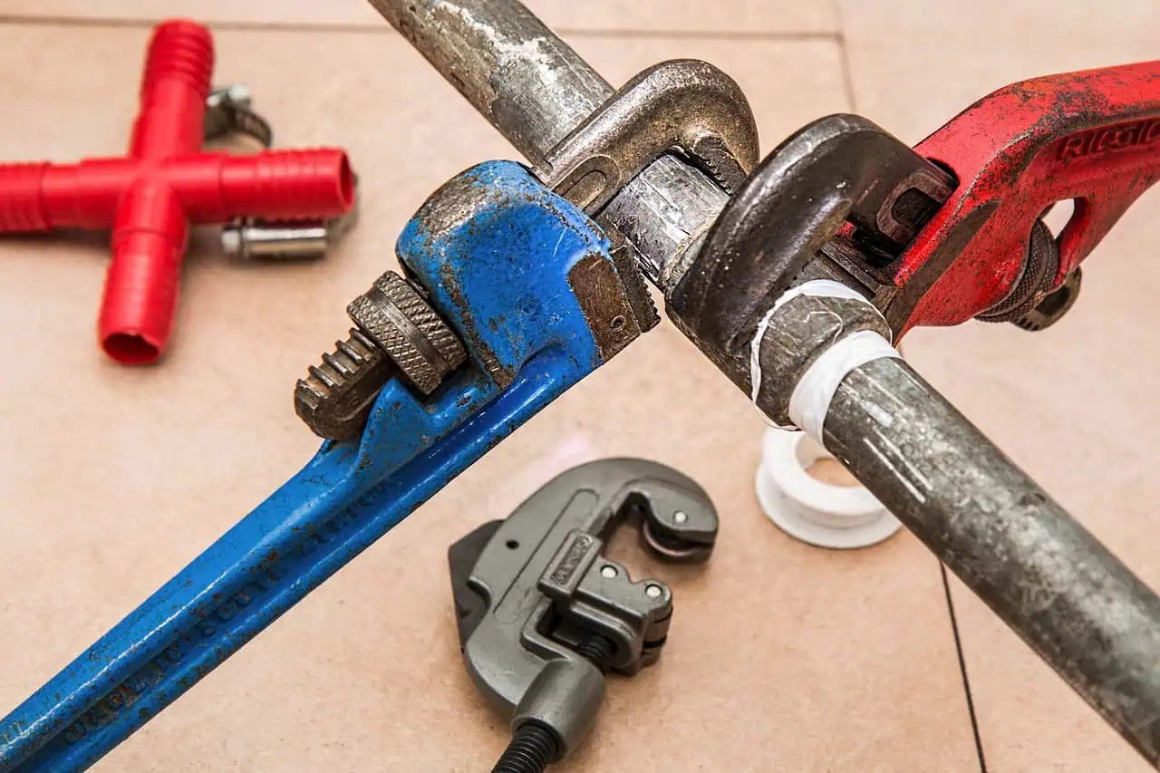 Clé à molette ajustée sur une canalisation de plomberie avec outils de réparation à proximité, illustration de services d'assurance pour travaux et réparations en Suisse.