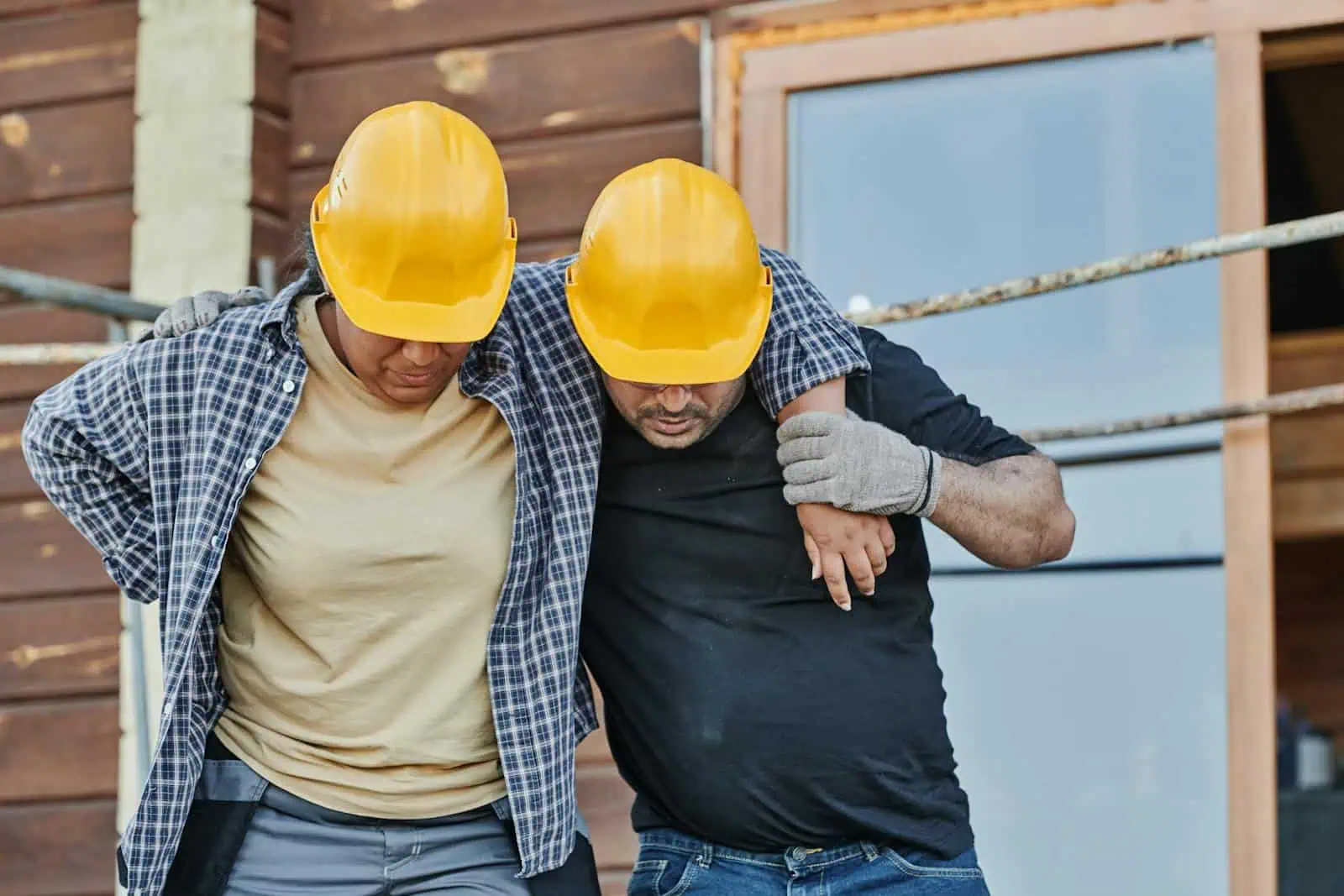 Souffrance au travail, deux ouvriers portant des casques de sécurité, aidant un collègue blessé à sortir d’un chantier, illustration pour assurance accidents professionnelles.