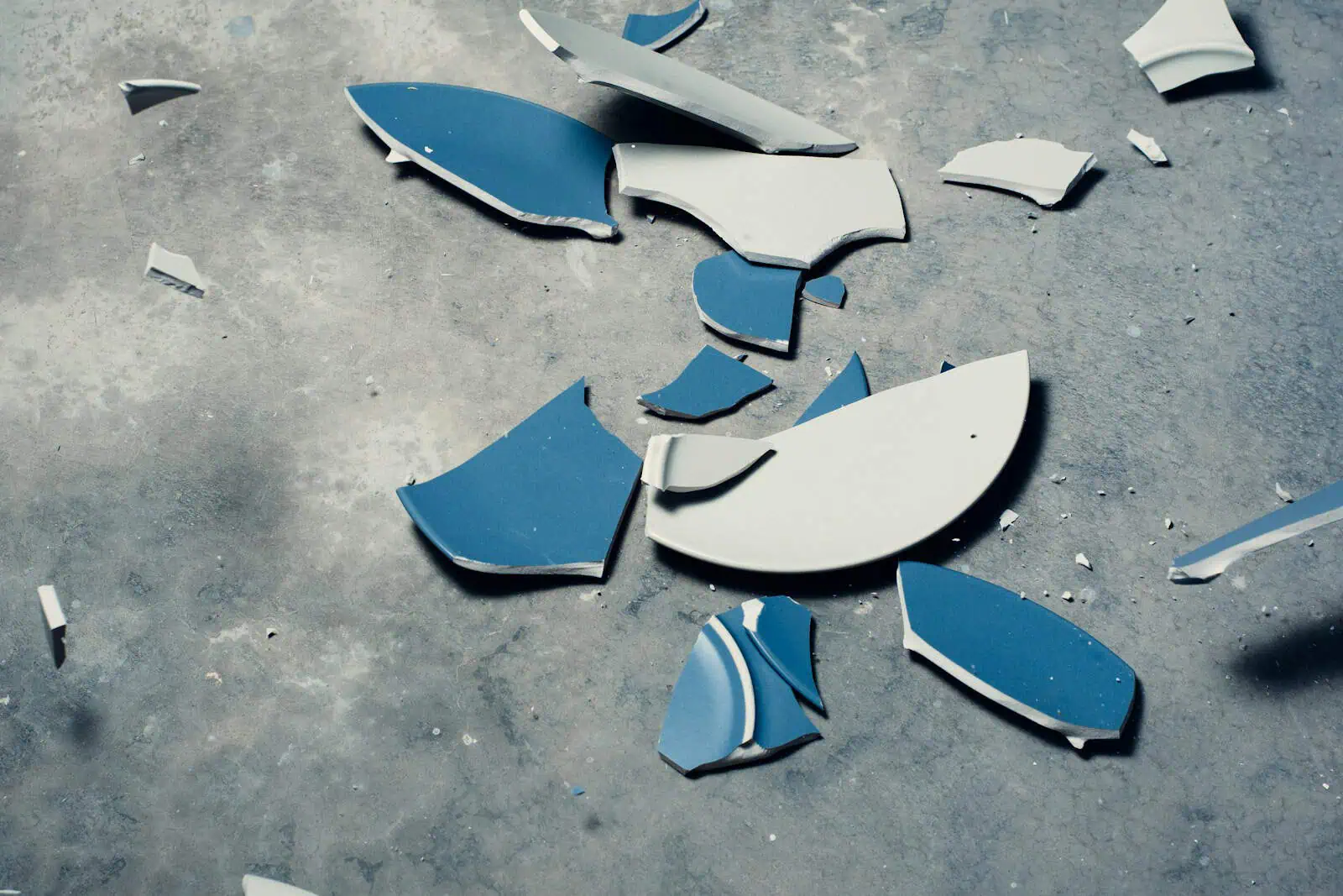 Fichiers cassés de carrelage ou de vaisselle sur sol en béton, illustrant un dommage accidentel ou une nécessité d'assurance.
