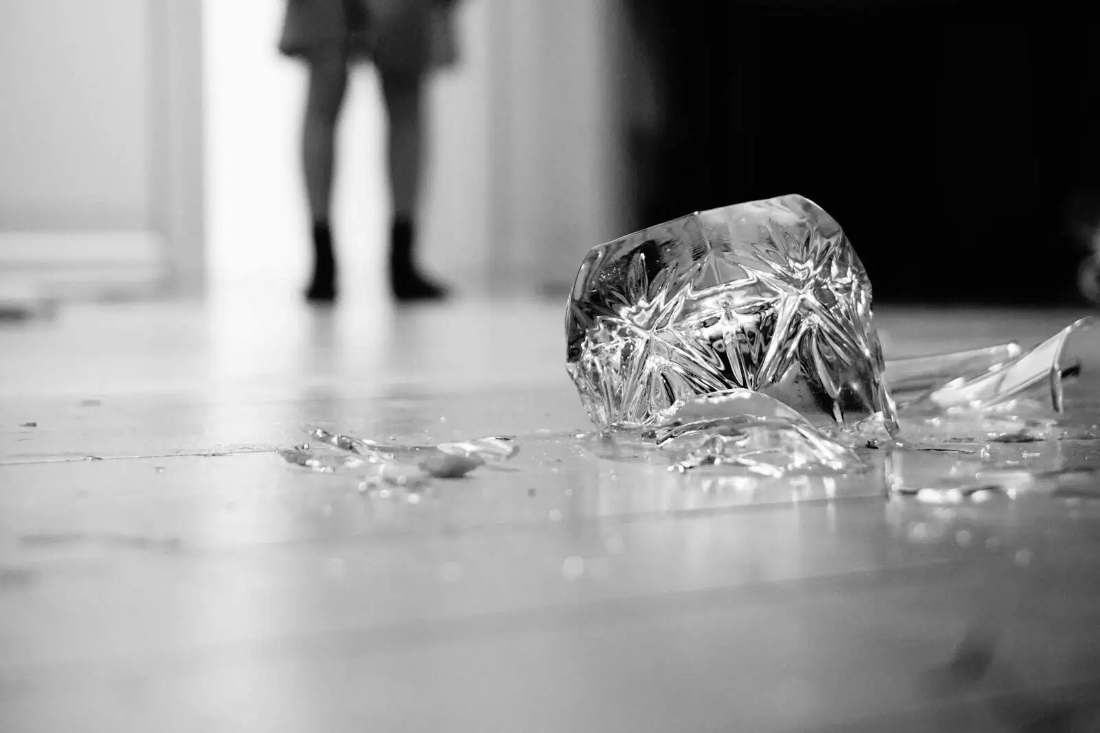 Verrre de verre cassé sur un sol, symbole d'accident domestique, avec des chaussures en arrière-plan.