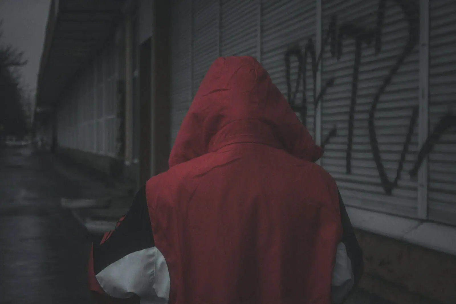 Vieux homme seul avec une capuche rouge, marche dans une rue sombre et vide, illustration de sécurité et d'assurance à Neuchâtel, conditions hivernales.