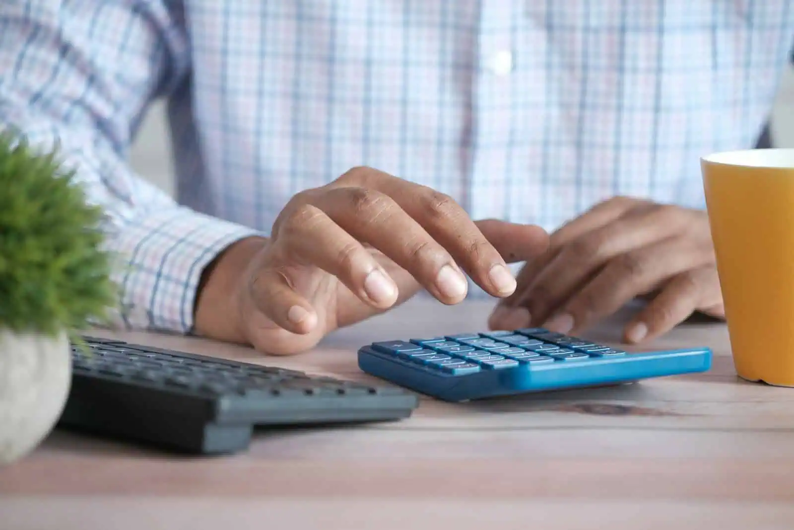 Calculatrice bancaire sur bureau avec main d'homme en chemise à carreaux, environnement professionnel, assurance, gestion financière.