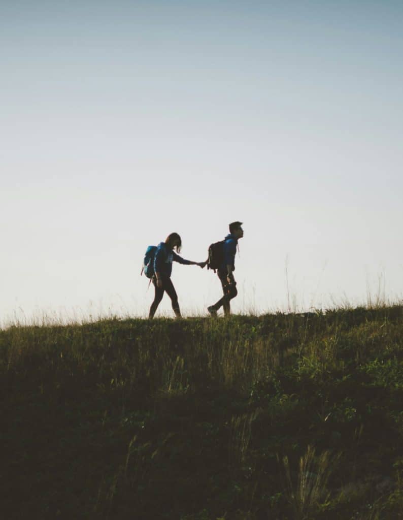 Voyage randonnée en nature avec deux personnes portant des sacs à dos, marche en plein air, silhouette contre ciel, aventure, protection assurée par Neuchâtel Assurances, sécurité et confiance.