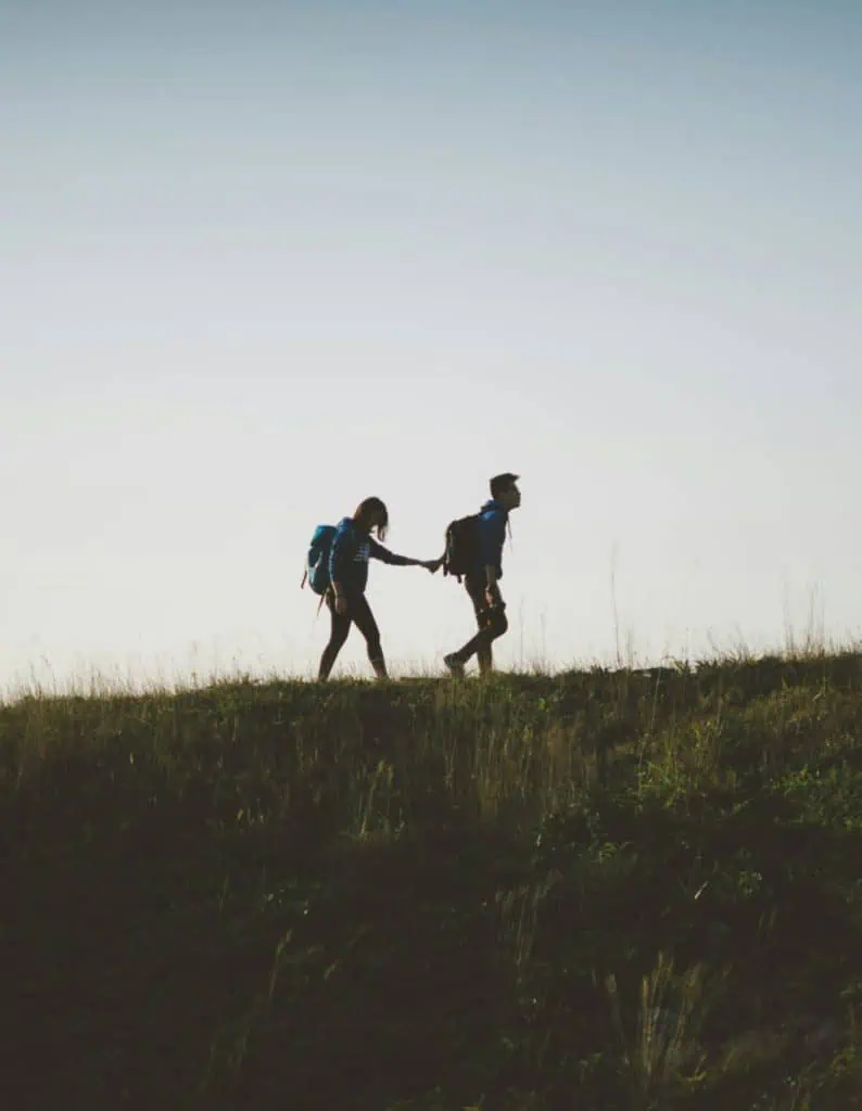 Voyage randonnée en nature avec deux personnes portant des sacs à dos, marche en plein air, silhouette contre ciel, aventure, protection assurée par Neuchâtel Assurances, sécurité et confiance.