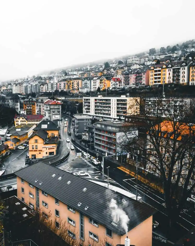 Villes de Neuchâtel en Suisse avec bâtiments résidentiels colorés, routes animées et paysage urbain, sous un ciel brumeux en hiver.