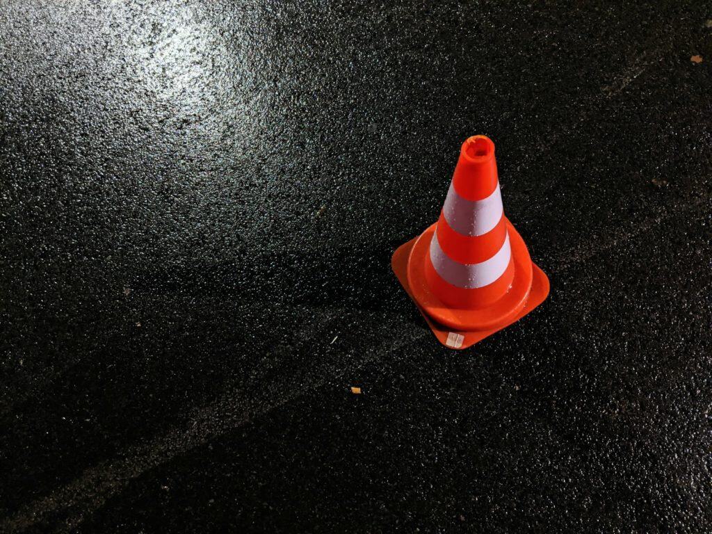 Cône de signalisation orange et blanc sur chaussée humide, sécurité et gestion des travaux ou des incidents routiers.