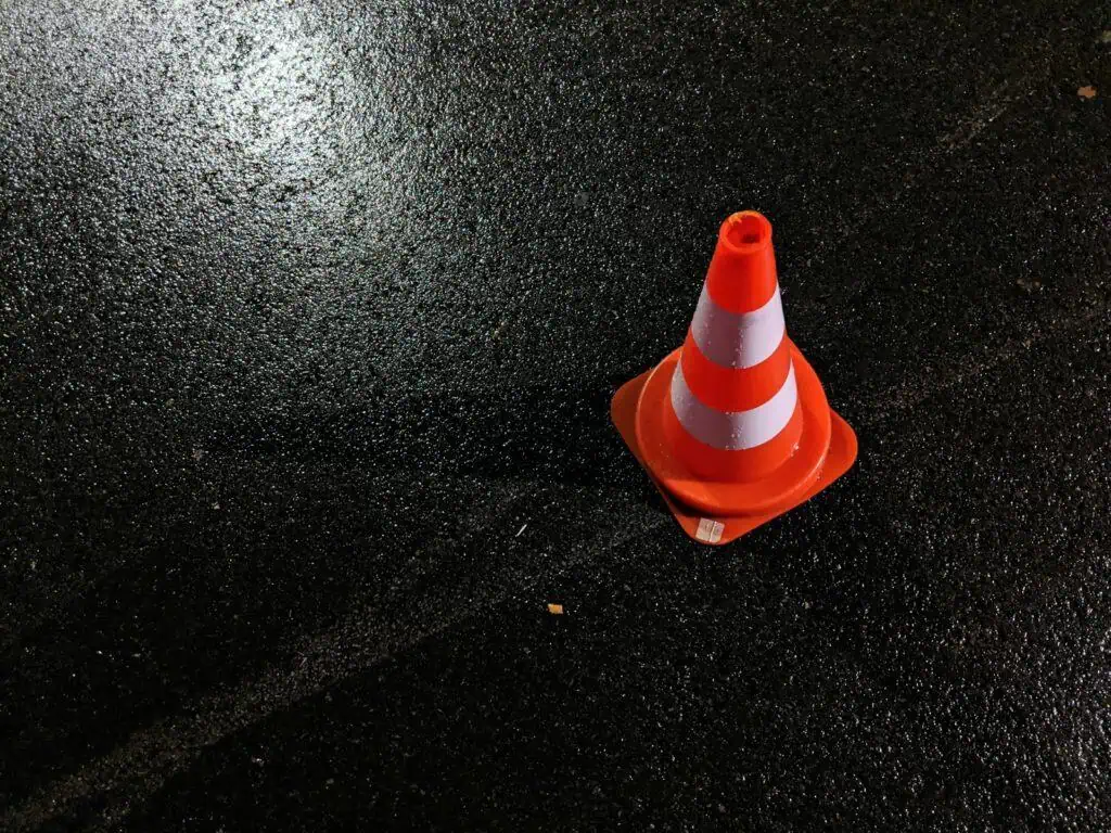 Cône de signalisation orange et blanc sur chaussée humide, sécurité et gestion des travaux ou des incidents routiers.