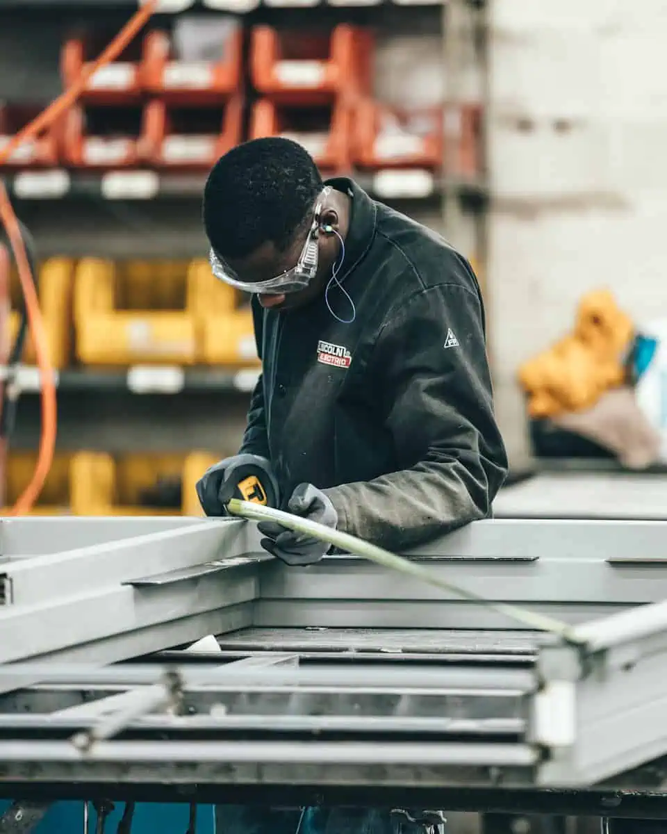 Technicien en usine portant équipement de protection travaillant sur un projet de fabrication industrielle.