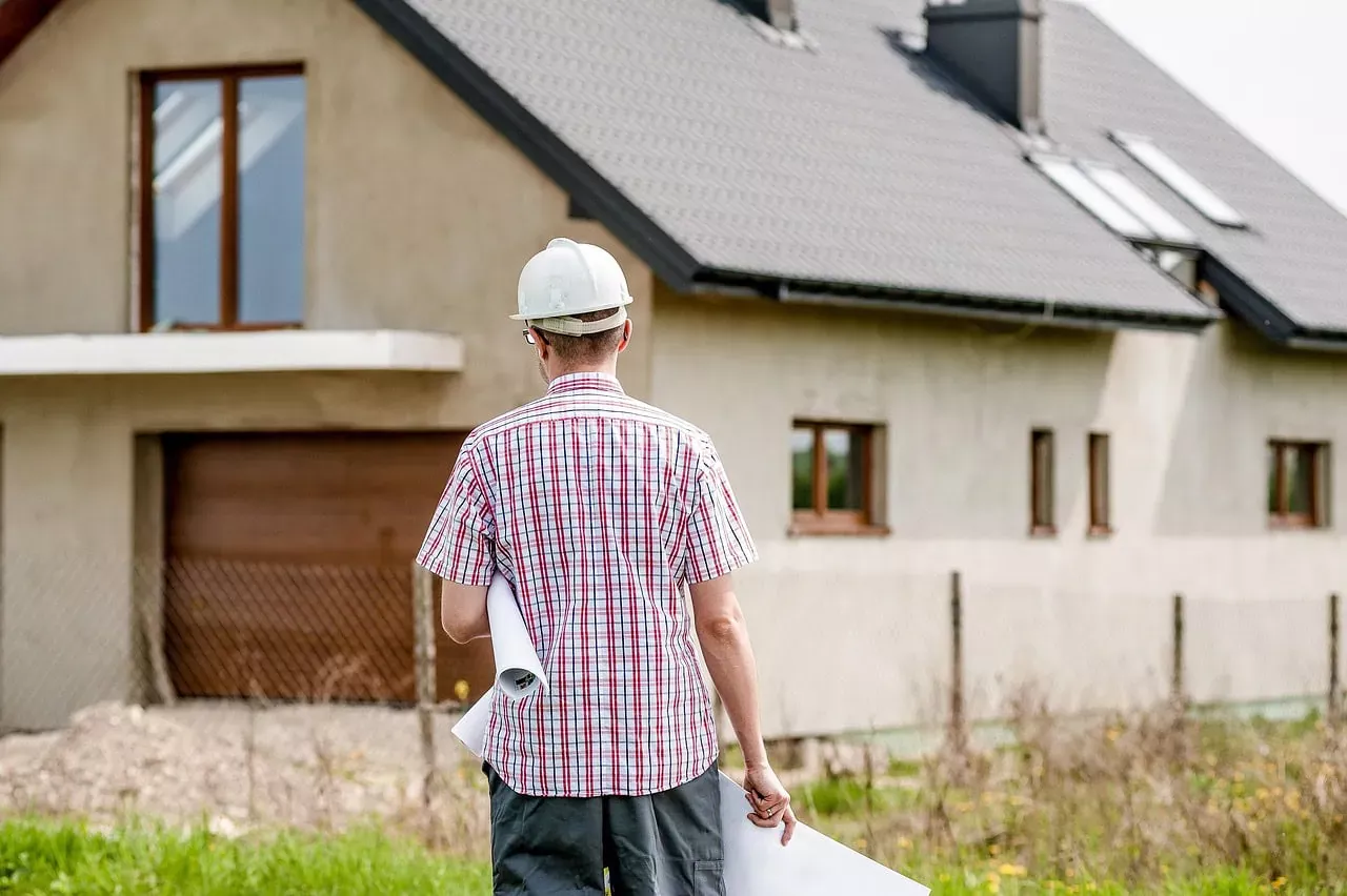Inspecteur en construction avec casque et plans devant une maison neuve à Neuchâtel, spécialiste des assurances habitation et construction.