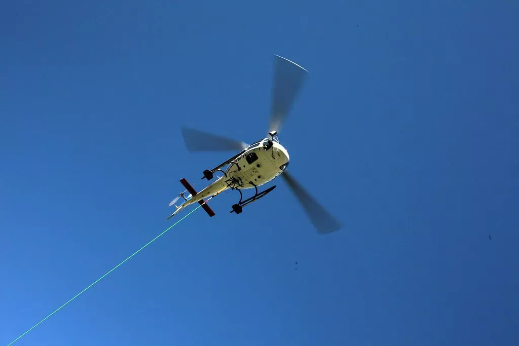 Hélicoptère en vol avec câble de levage contre un ciel bleu clair, symbolisant la sécurité et l'intervention aérienne.