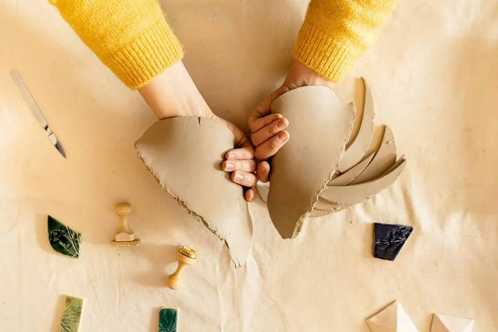 Poinçonnées en céramique craquelée par deux mains, symbolisant la solidité et la fiabilité des assurances Neuchâtel, avec outils et échantillons en arrière-plan, représentant la personnalisation et la qualité du service.