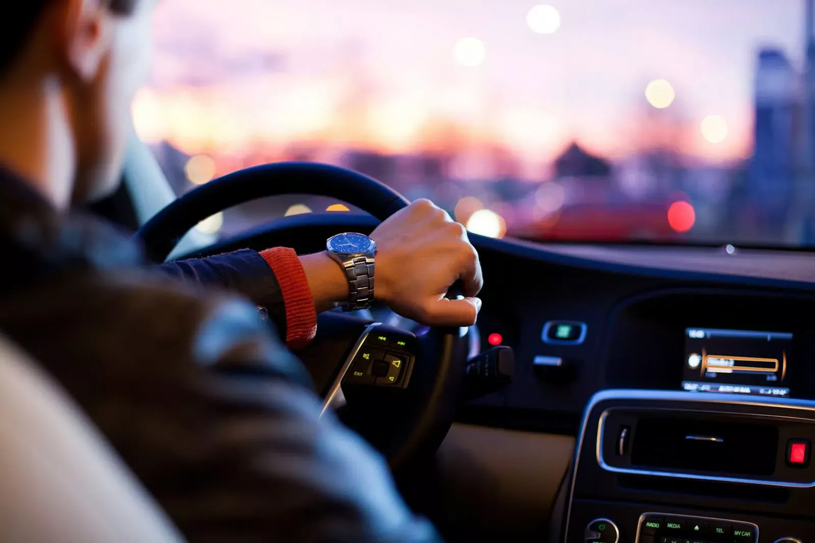 Conducteur au volant d'une voiture moderne avec tableau de bord numérique, au coucher de soleil, promotion des assurances auto à Neuchâtel.