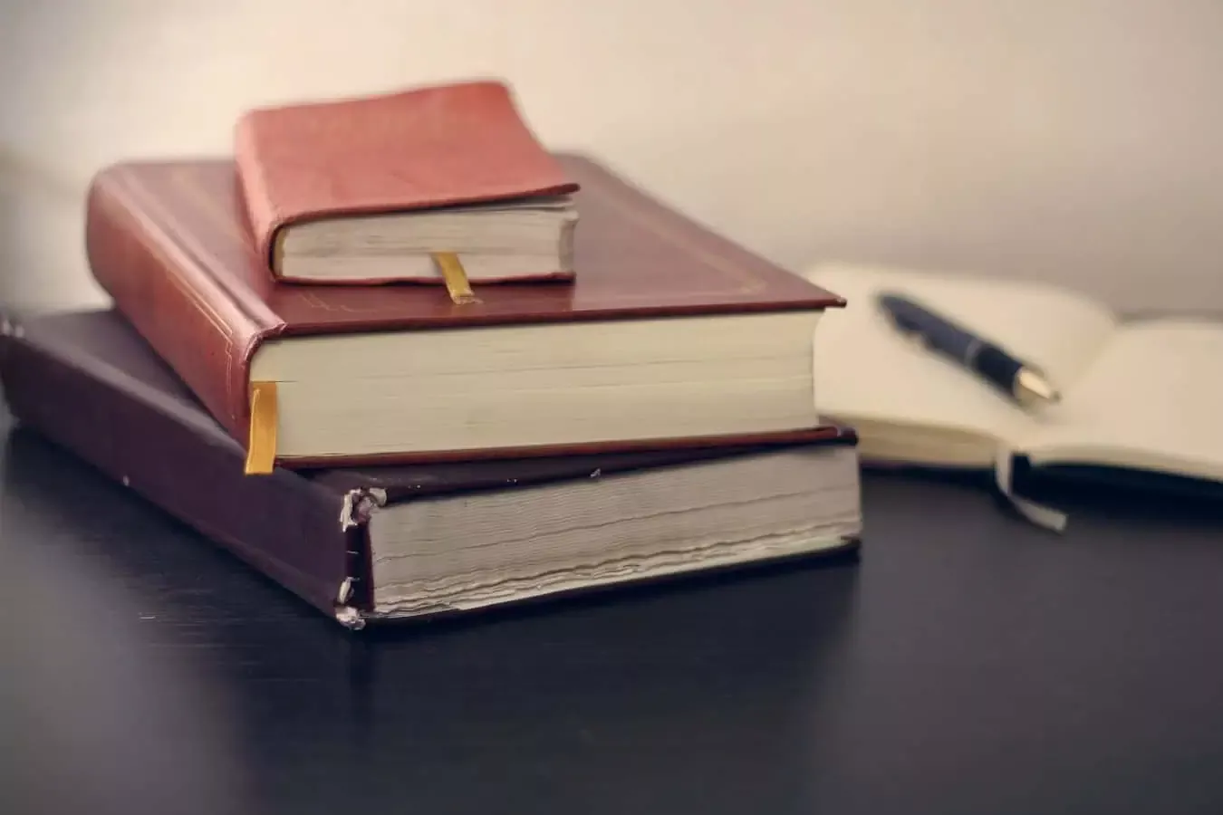 Cahiers et agenda en cuir rouge empilés sur un bureau, avec un stylo et un carnet blanc ouvert à côté, évoquant organisation, planification et assurance à Neuchâtel.