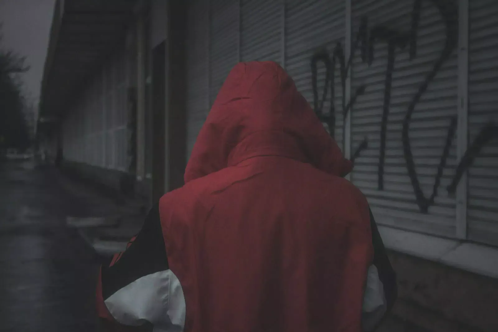 Vieux homme seul avec une capuche rouge, marche dans une rue sombre et vide, illustration de sécurité et d'assurance à Neuchâtel, conditions hivernales.