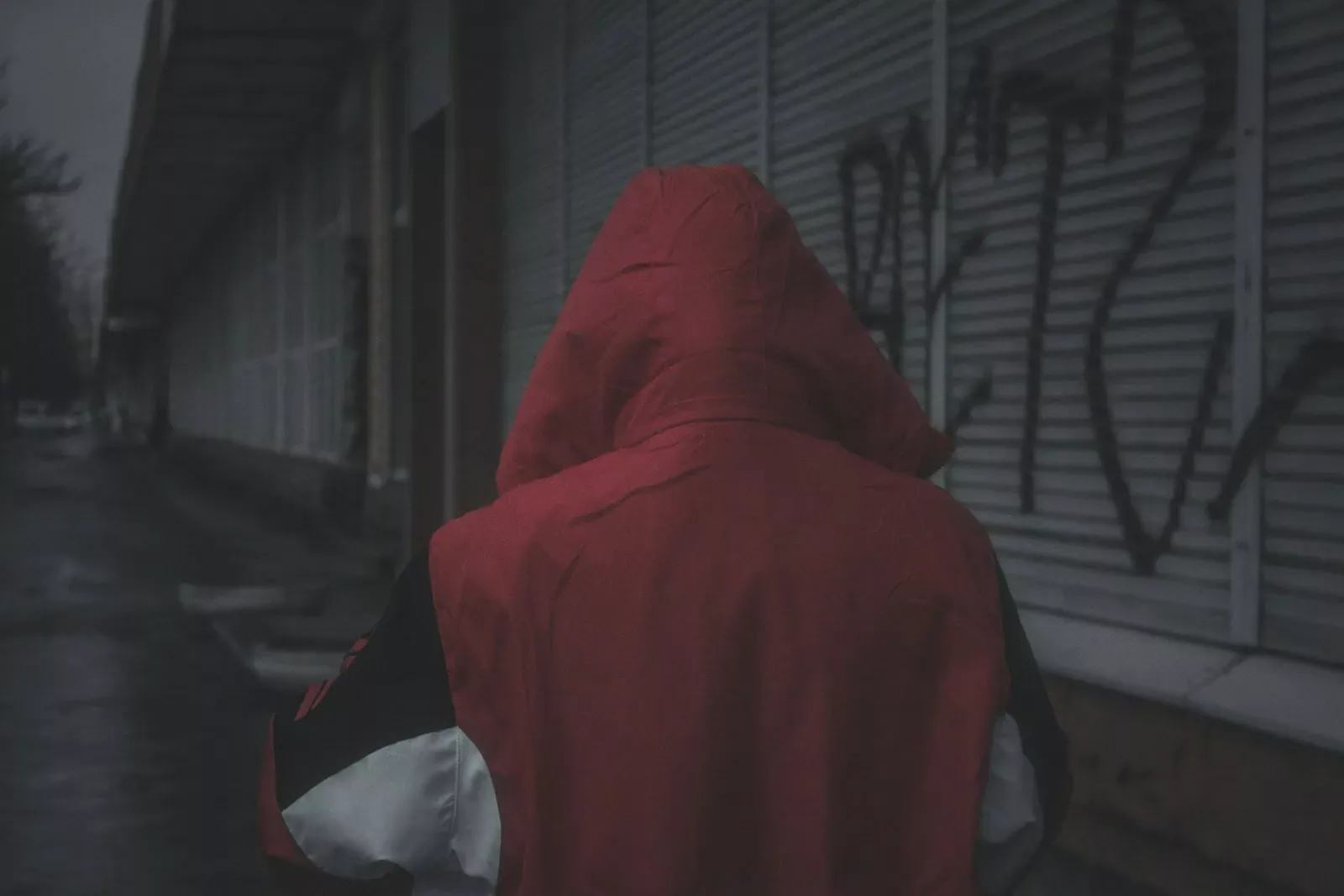 Vieux homme seul avec une capuche rouge, marche dans une rue sombre et vide, illustration de sécurité et d'assurance à Neuchâtel, conditions hivernales.