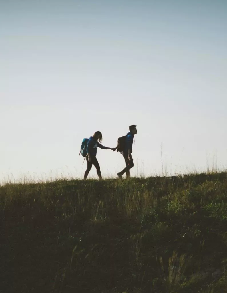 Voyage randonnée en nature avec deux personnes portant des sacs à dos, marche en plein air, silhouette contre ciel, aventure, protection assurée par Neuchâtel Assurances, sécurité et confiance.