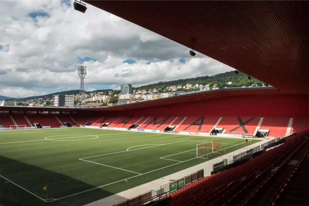 Stade de football à Neuchâtel, vue depuis les gradins, avec la ville et les collines en arrière-plan, sous un ciel nuageux, illustrant l'assurance sportive et la sécurité des infrastructures.