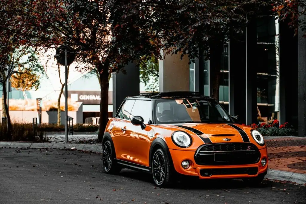 Mini Cooper orange et noire garée devant un bâtiment moderne avec des arbres automnaux.