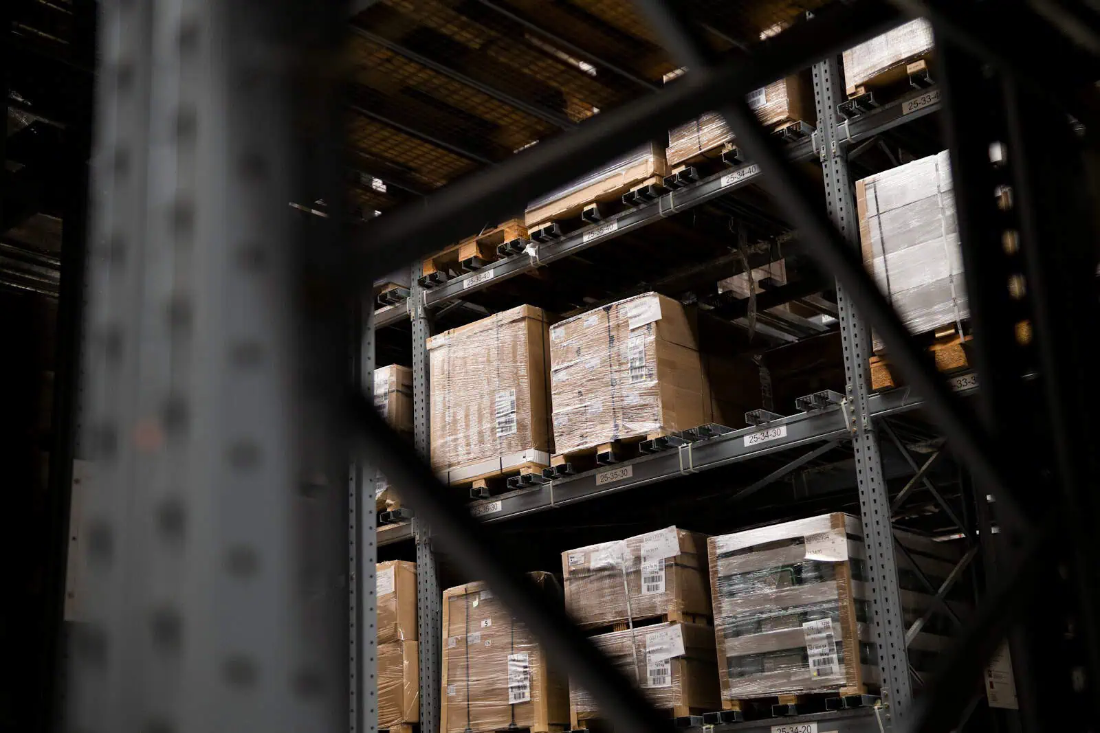 Palettes en carton dans un entrepôt, vues à travers une étagère métallique, stockage sécurisé pour l'assurance et la logistique, images illustrant la gestion des stocks.