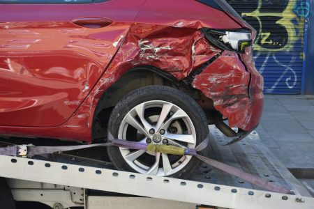 Dommage à une voiture rouge suite à un accident, voiture attelée sur une remorque, véhicule endommagé avant droit, accident, réparation, assurance auto.